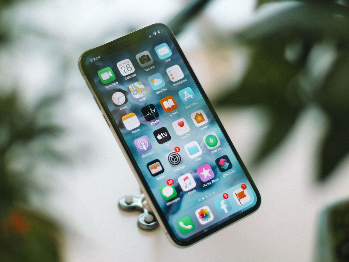 An iPhone displaying its home screen of app icons, clipped to a holder against a blurred green leafy background